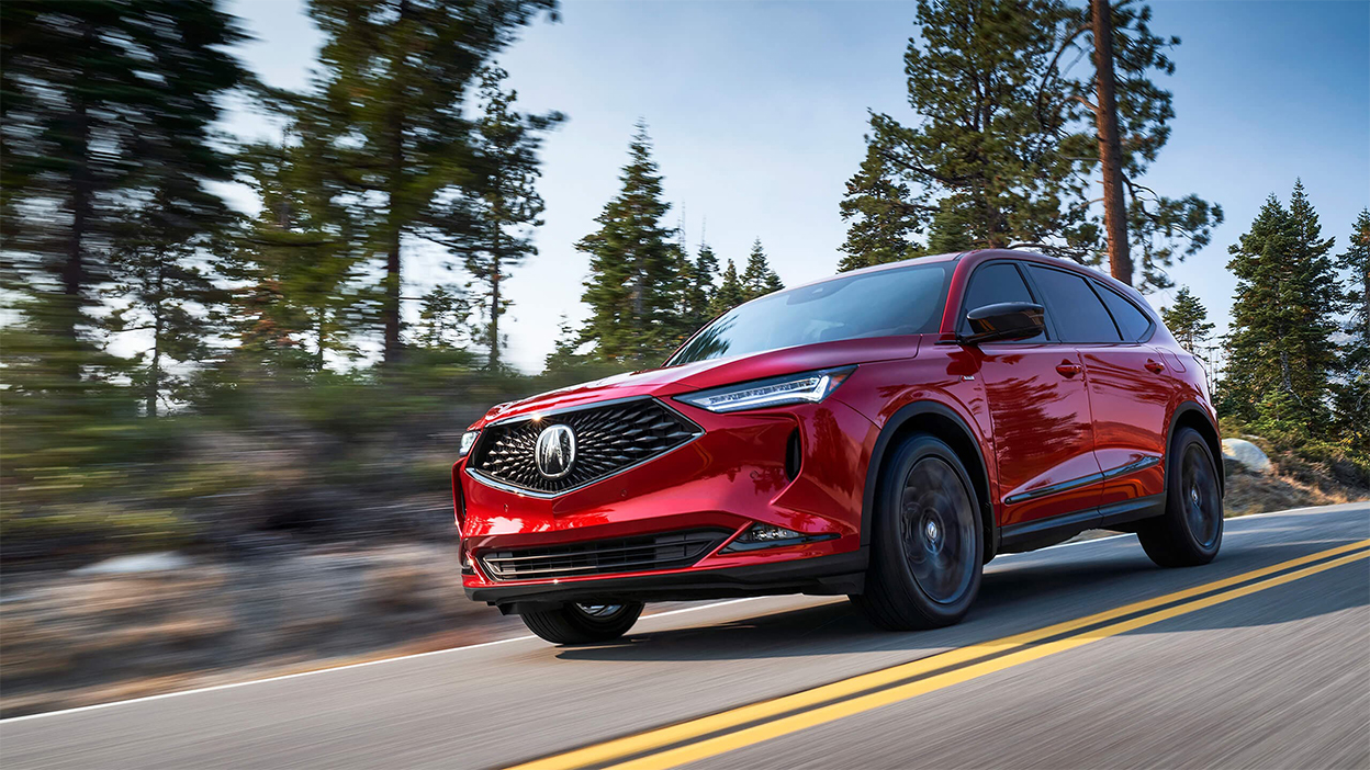 A red MDX drives down a road in the wilderness.