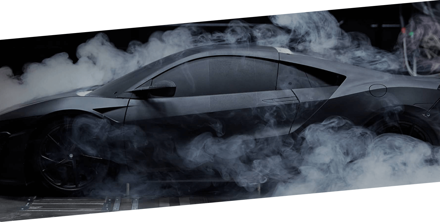 A Black Acura NSX spinning its rear wheels and producing smoke. / Une Acura NSX noire crée un nuage de fumée avec ses roues arrière.